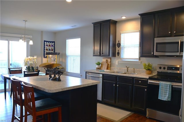 kitchen with sink, dark hardwood / wood-style flooring, a kitchen island, pendant lighting, and stainless steel appliances