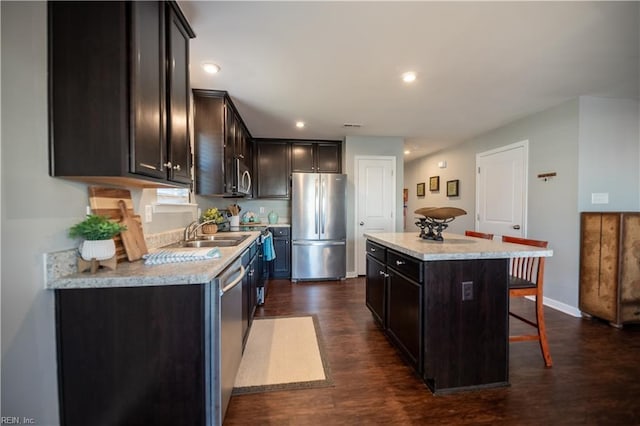 kitchen featuring sink, dark wood-type flooring, appliances with stainless steel finishes, a center island, and a kitchen bar