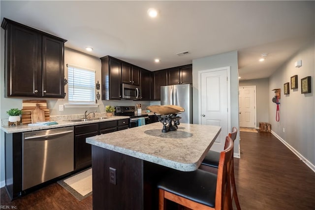 kitchen with appliances with stainless steel finishes, sink, a breakfast bar area, a center island, and dark wood-type flooring