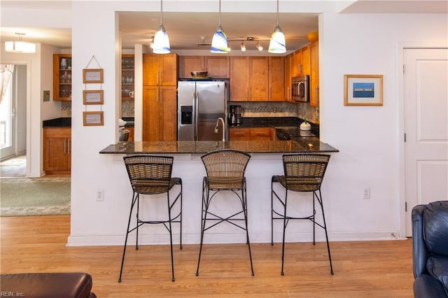 kitchen with pendant lighting, stainless steel appliances, kitchen peninsula, and dark stone counters