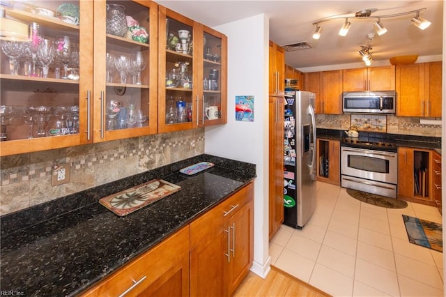 kitchen featuring decorative backsplash, stainless steel appliances, dark stone counters, and light tile patterned flooring