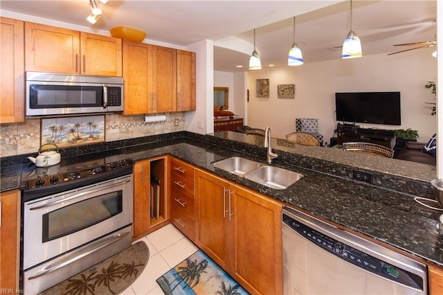 kitchen with sink, light tile patterned floors, appliances with stainless steel finishes, decorative light fixtures, and dark stone counters