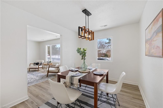 dining area with a healthy amount of sunlight, a chandelier, and light hardwood / wood-style floors