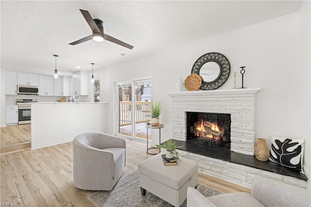 living room with ceiling fan, a fireplace, light hardwood / wood-style flooring, and a textured ceiling