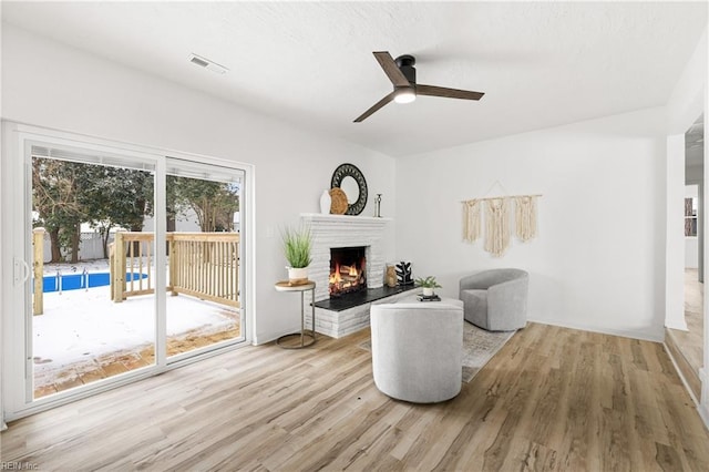 living area featuring ceiling fan, a brick fireplace, and light wood-type flooring