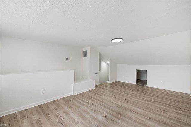 bonus room featuring lofted ceiling, a textured ceiling, and light hardwood / wood-style floors