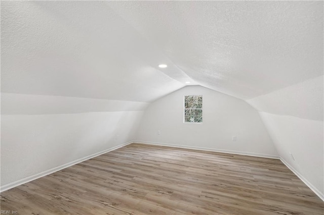 additional living space featuring hardwood / wood-style flooring, lofted ceiling, and a textured ceiling