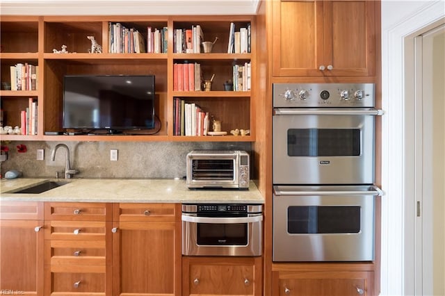 kitchen featuring light stone counters, sink, double oven, and tasteful backsplash