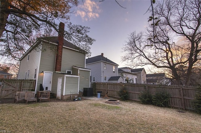 back house at dusk featuring a lawn, central AC, and an outdoor fire pit