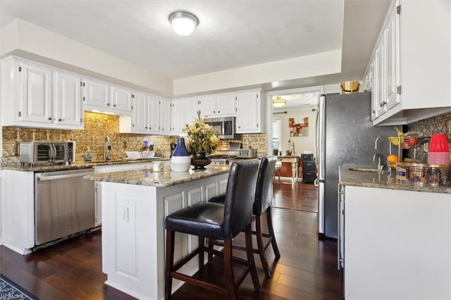 kitchen featuring stone counters, white cabinetry, appliances with stainless steel finishes, and a center island