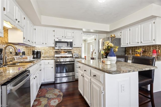 kitchen featuring sink, a kitchen island, stone counters, stainless steel appliances, and white cabinets