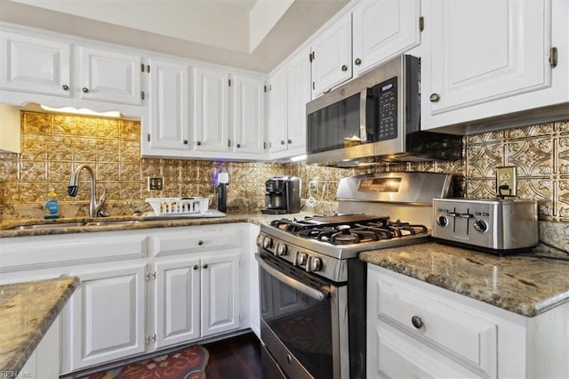 kitchen with white cabinetry, stainless steel appliances, backsplash, and dark stone countertops