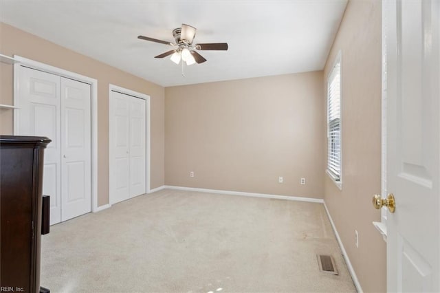 unfurnished bedroom with multiple closets, light carpet, and ceiling fan