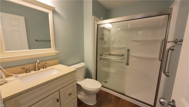 bathroom featuring vanity, wood-type flooring, a shower with shower door, and toilet