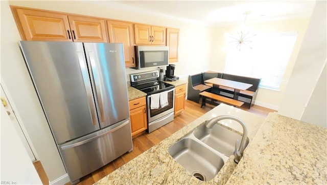 kitchen with sink, light stone counters, light wood-type flooring, a notable chandelier, and stainless steel appliances