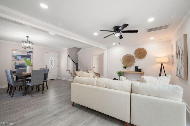 living room with ceiling fan with notable chandelier, ornamental molding, and hardwood / wood-style floors