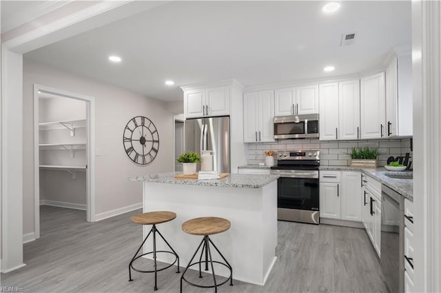 kitchen featuring white cabinetry, light stone counters, stainless steel appliances, and a kitchen island