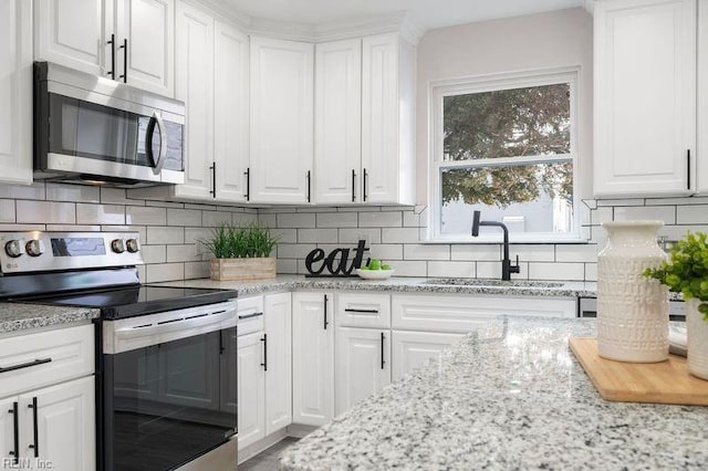 kitchen with appliances with stainless steel finishes, tasteful backsplash, sink, white cabinets, and light stone countertops