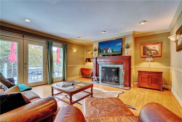 living room featuring crown molding, a premium fireplace, light hardwood / wood-style flooring, and french doors