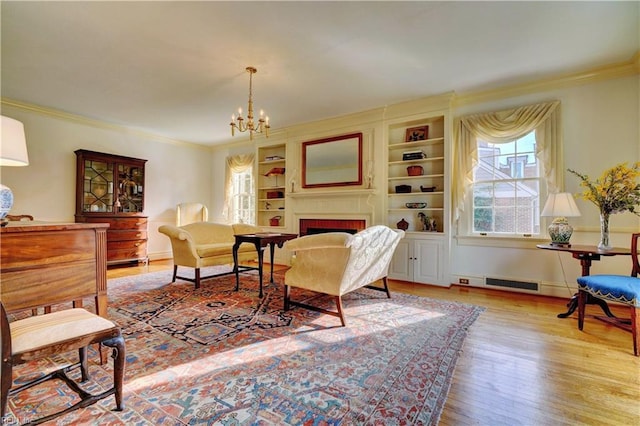 living area featuring crown molding, built in features, an inviting chandelier, a fireplace, and light wood-type flooring