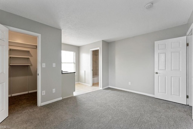 unfurnished bedroom with connected bathroom, a spacious closet, a textured ceiling, a closet, and light colored carpet