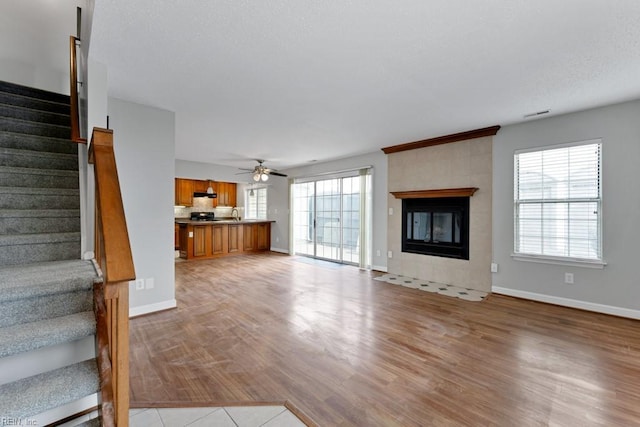 unfurnished living room with a fireplace, a wealth of natural light, ceiling fan, and light wood-type flooring