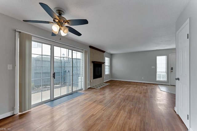 unfurnished living room featuring ceiling fan, a large fireplace, plenty of natural light, and wood-type flooring