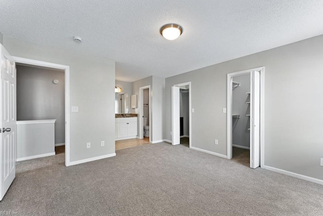 unfurnished bedroom featuring connected bathroom, a walk in closet, carpet, a textured ceiling, and a closet