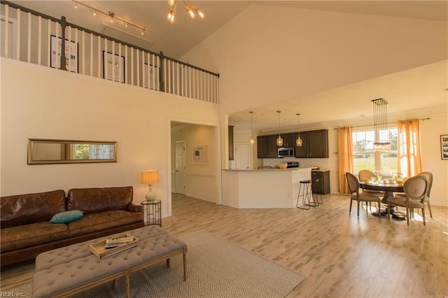 living room with an inviting chandelier, high vaulted ceiling, and light wood-type flooring