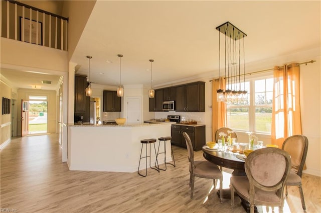 kitchen with crown molding, dark brown cabinets, pendant lighting, and light wood-type flooring