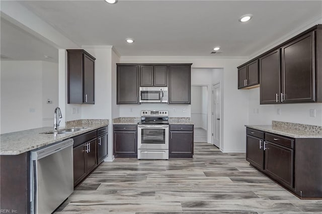 kitchen featuring sink, crown molding, dark brown cabinets, stainless steel appliances, and light stone countertops