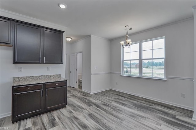 kitchen with hanging light fixtures, a notable chandelier, light hardwood / wood-style floors, ornamental molding, and light stone countertops