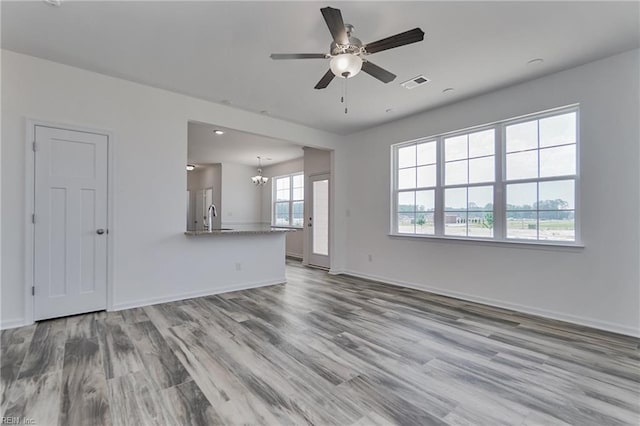 unfurnished living room with sink, ceiling fan with notable chandelier, and light hardwood / wood-style flooring