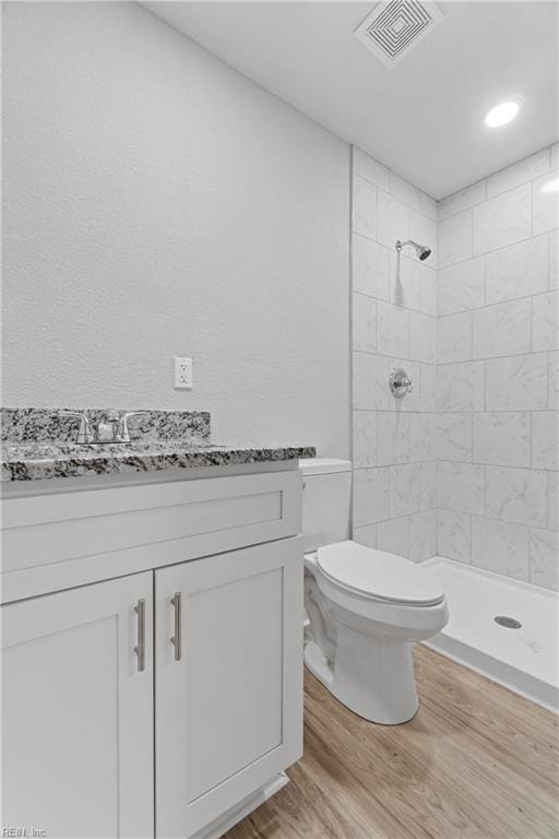 bathroom with wood-type flooring, a tile shower, vanity, and toilet