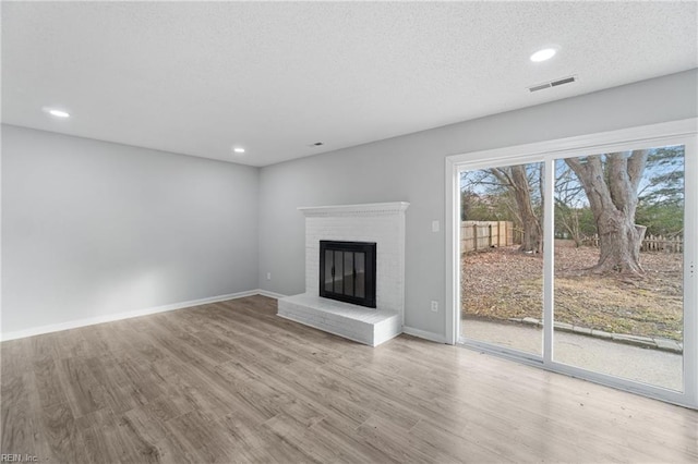 unfurnished living room with a healthy amount of sunlight, a textured ceiling, a fireplace, and light hardwood / wood-style flooring