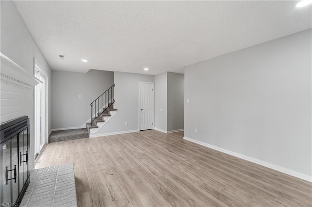 unfurnished living room with a brick fireplace, a textured ceiling, and light hardwood / wood-style flooring