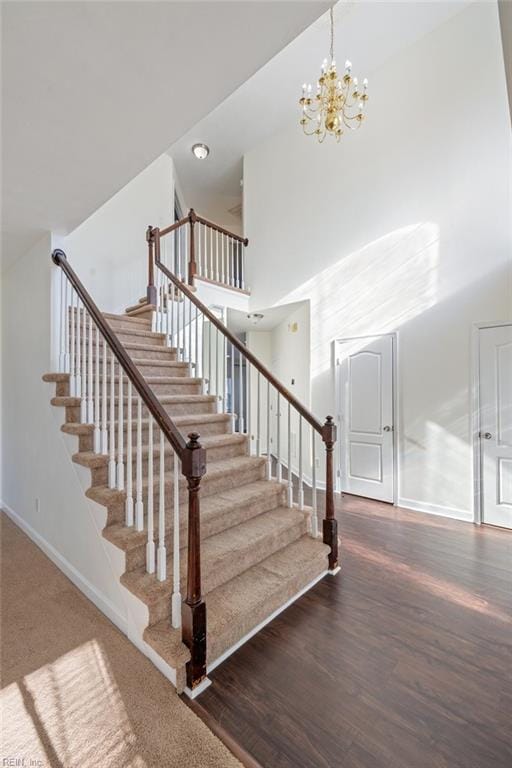 stairs featuring an inviting chandelier, wood-type flooring, and a high ceiling