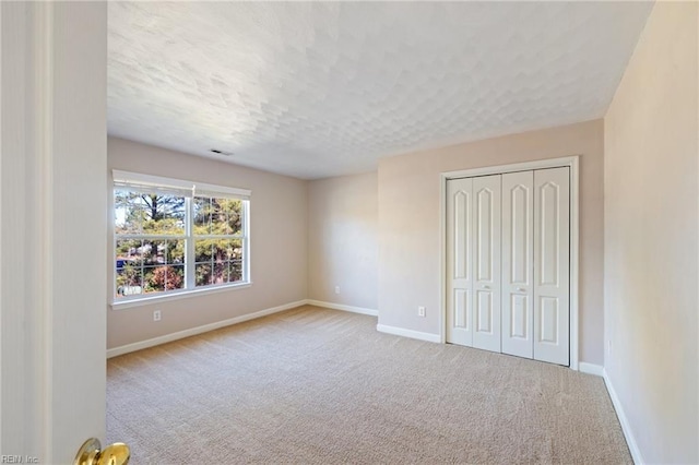 unfurnished bedroom featuring light colored carpet, a closet, and a textured ceiling