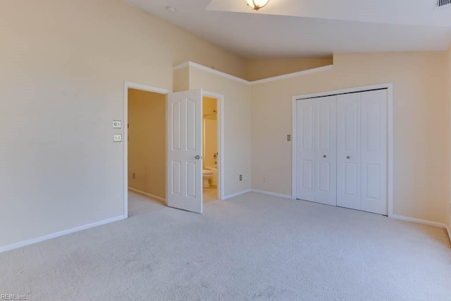 unfurnished bedroom featuring lofted ceiling, ensuite bath, light colored carpet, and a closet