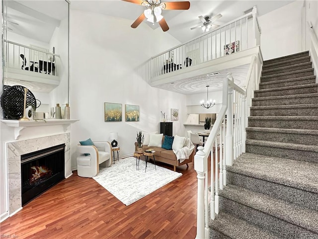 living room featuring ceiling fan with notable chandelier, a towering ceiling, a high end fireplace, and hardwood / wood-style floors