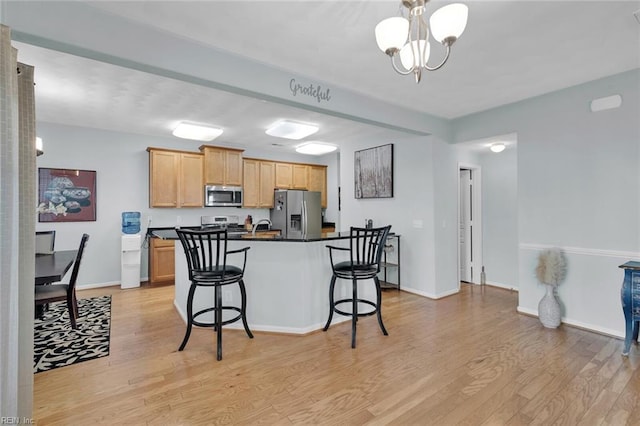 kitchen featuring a breakfast bar, a chandelier, stainless steel appliances, light brown cabinets, and light hardwood / wood-style flooring