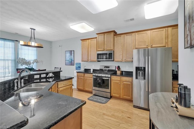 kitchen featuring sink, decorative light fixtures, dark stone countertops, light wood-type flooring, and stainless steel appliances