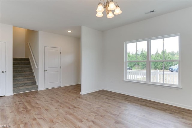 spare room with a notable chandelier and light wood-type flooring