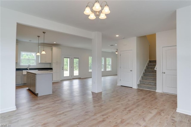 unfurnished living room featuring plenty of natural light, ceiling fan with notable chandelier, and light hardwood / wood-style floors