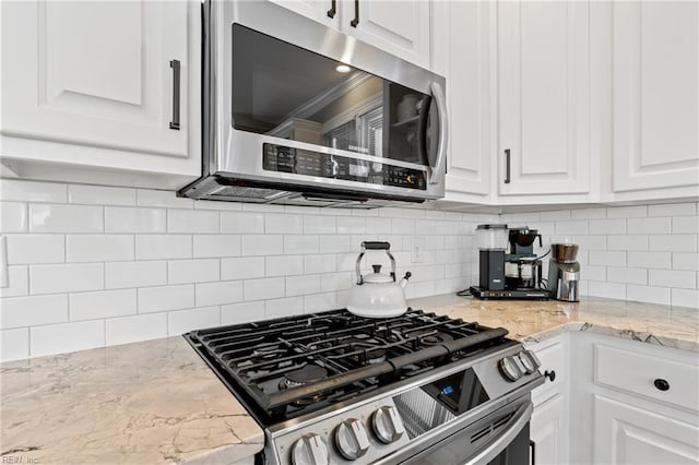 kitchen with tasteful backsplash, white cabinetry, stainless steel appliances, and light stone countertops