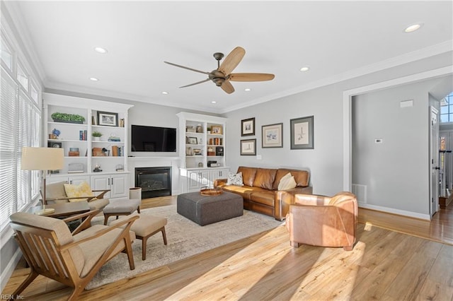 living room featuring built in shelves, ceiling fan, ornamental molding, and light hardwood / wood-style flooring