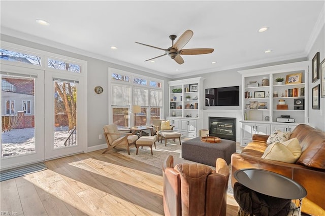 living room featuring crown molding, ceiling fan, built in shelves, and light hardwood / wood-style floors