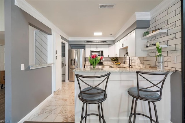 kitchen featuring appliances with stainless steel finishes, white cabinetry, sink, kitchen peninsula, and light stone countertops