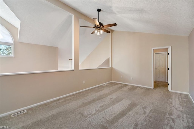 empty room with lofted ceiling, a textured ceiling, light colored carpet, and ceiling fan