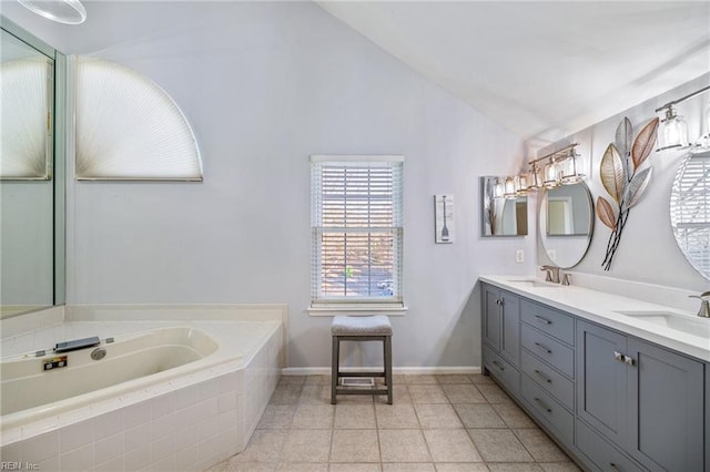 bathroom with tile patterned flooring, vanity, lofted ceiling, and tiled bath